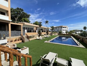 Un resort moderno con piscina, césped artificial y sillones de descanso.