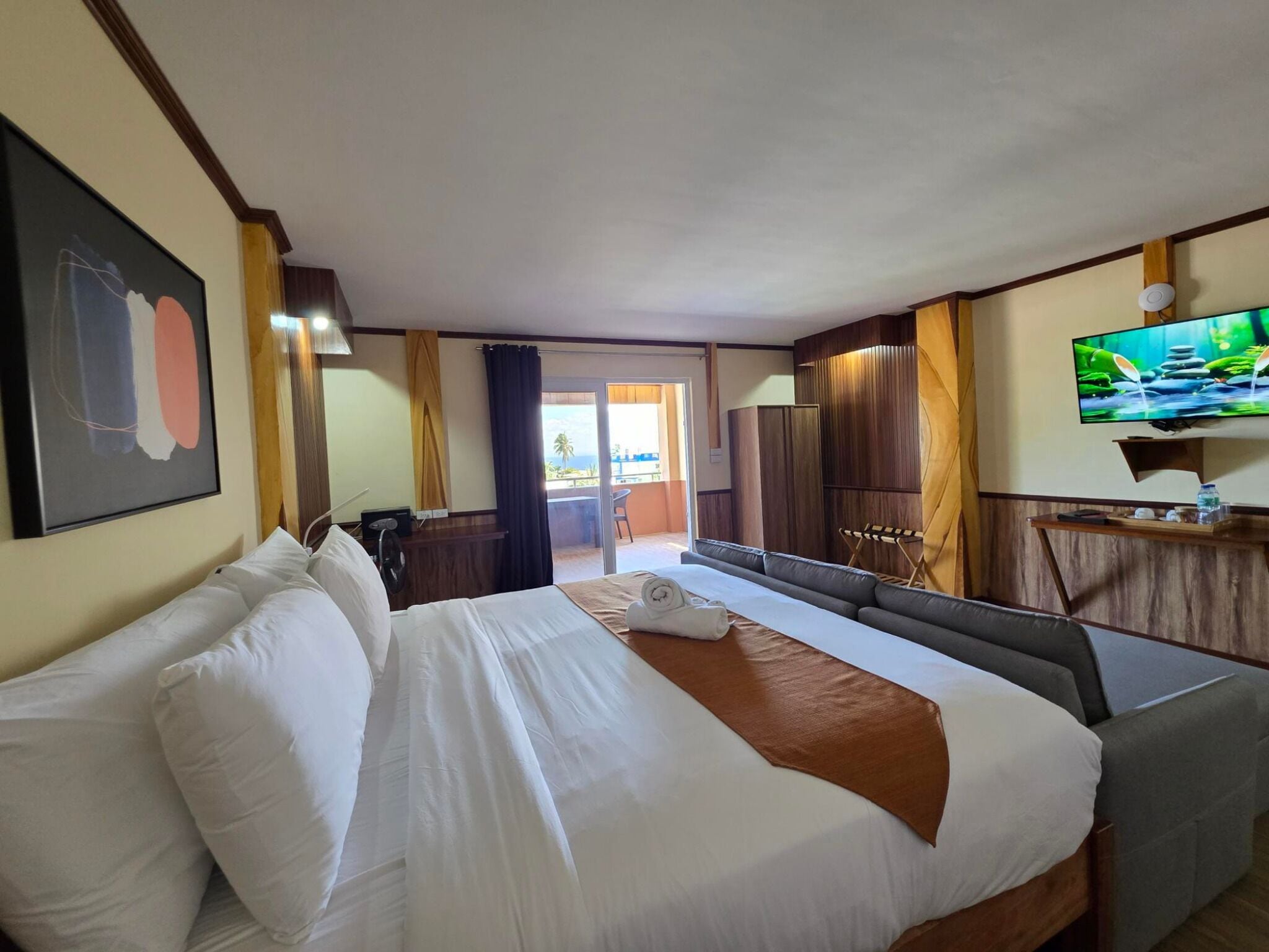 A hotel room with a large bed, a TV, and a view of the outdoors.