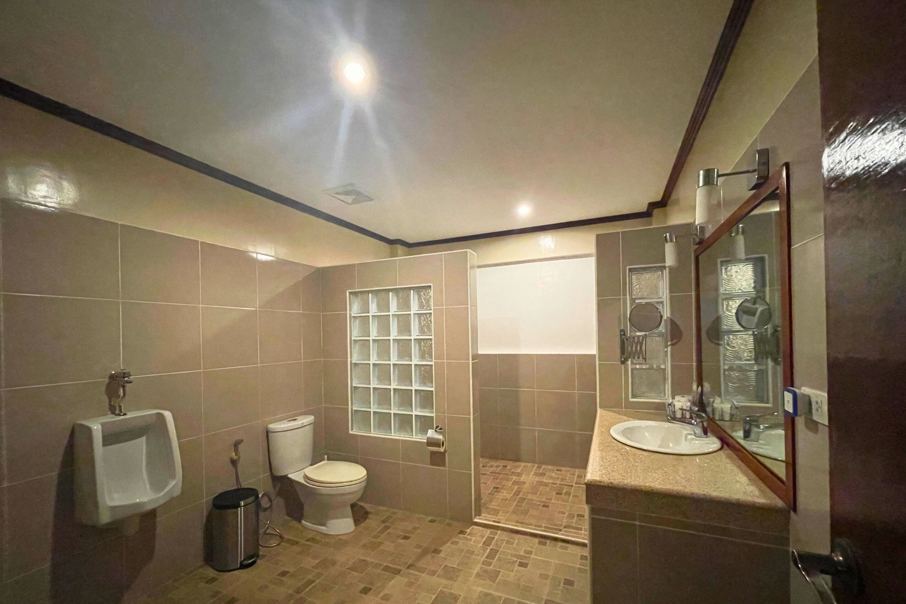 Un baño con orinal, inodoro, lavamanos y un espejo grande.