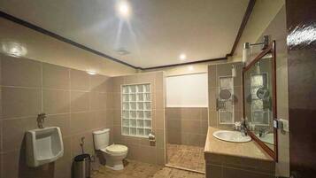 Un baño con orinal, inodoro, lavamanos y un espejo grande.