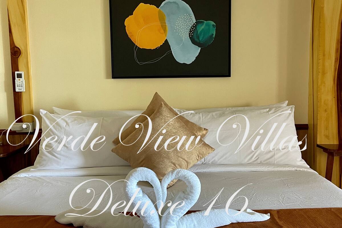 A hotel room with a bed, pillows, and a wall art piece.