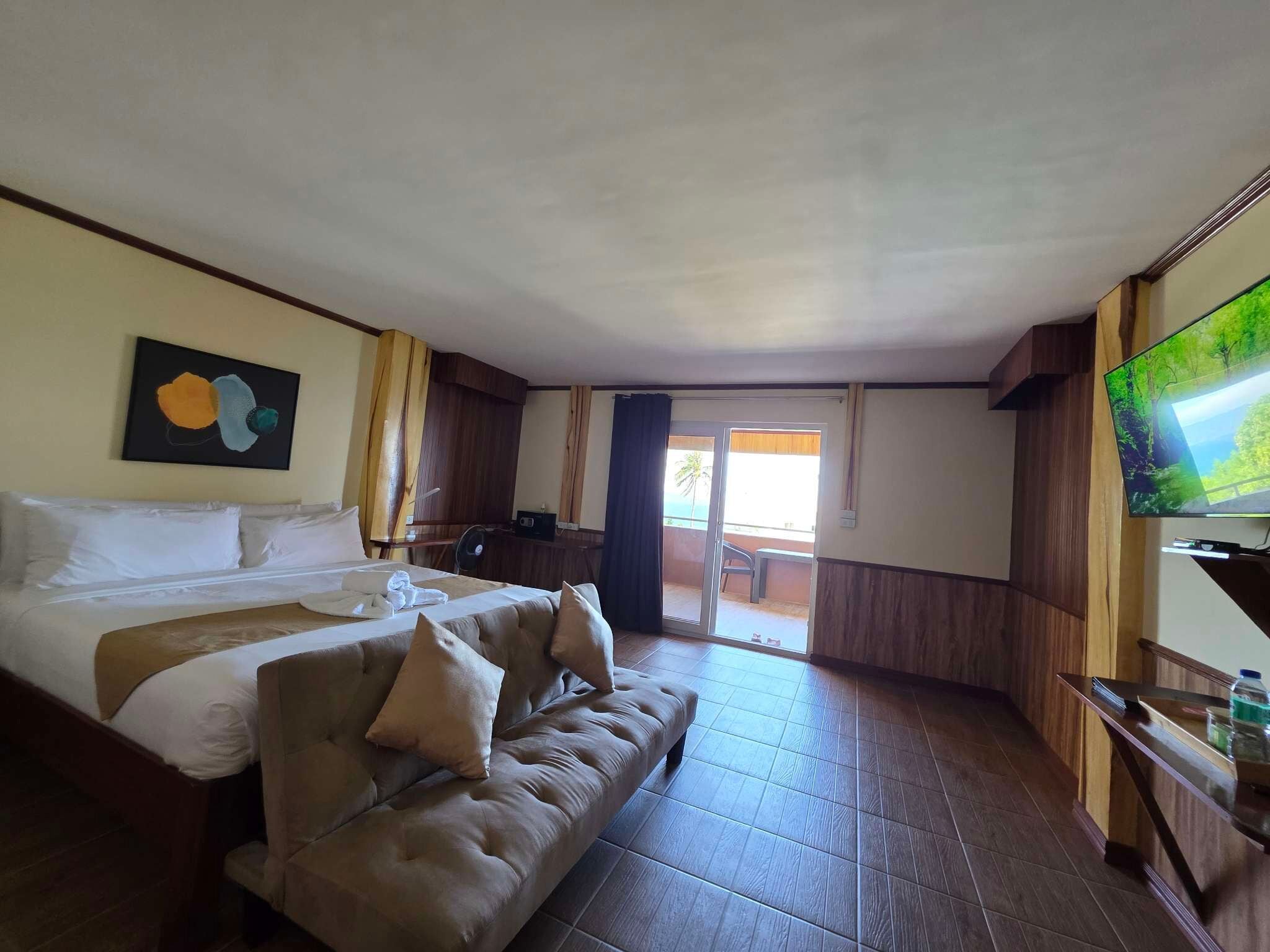 A hotel room with a bed, a sofa, a TV, and a sliding door to the outside.