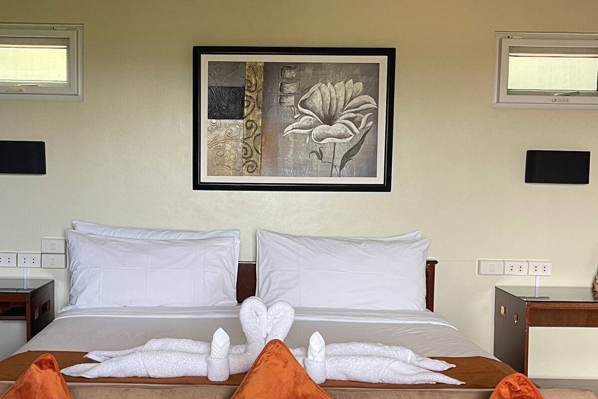 A hotel room with a bed, two bedside tables, a framed artwork above the bed, and two wall-mounted lights.