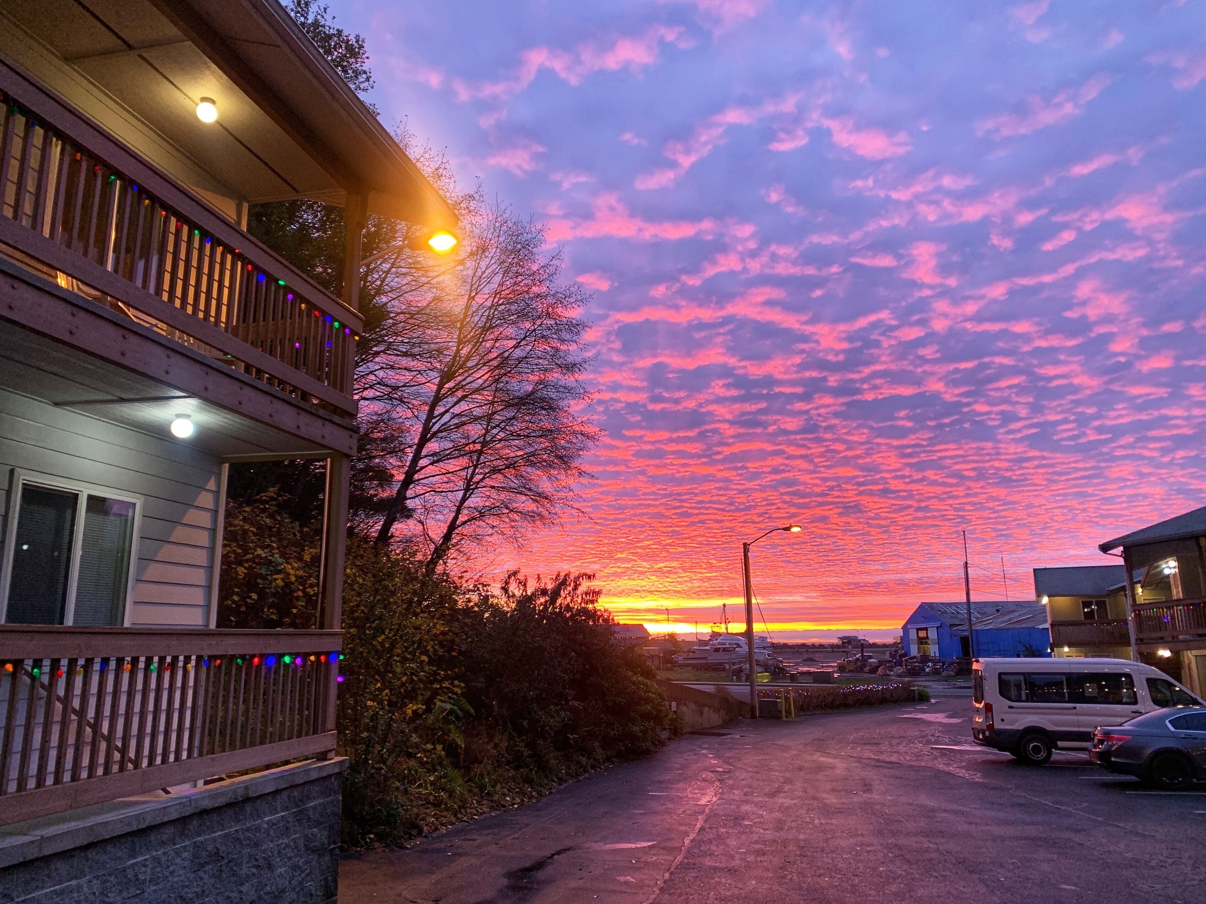 A residential street with a sunset, a wooden deck, and a parked van.