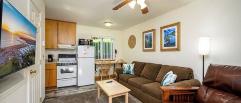 A compact living space with a kitchenette, a brown leather sofa, a wooden coffee table, and a ceiling fan.