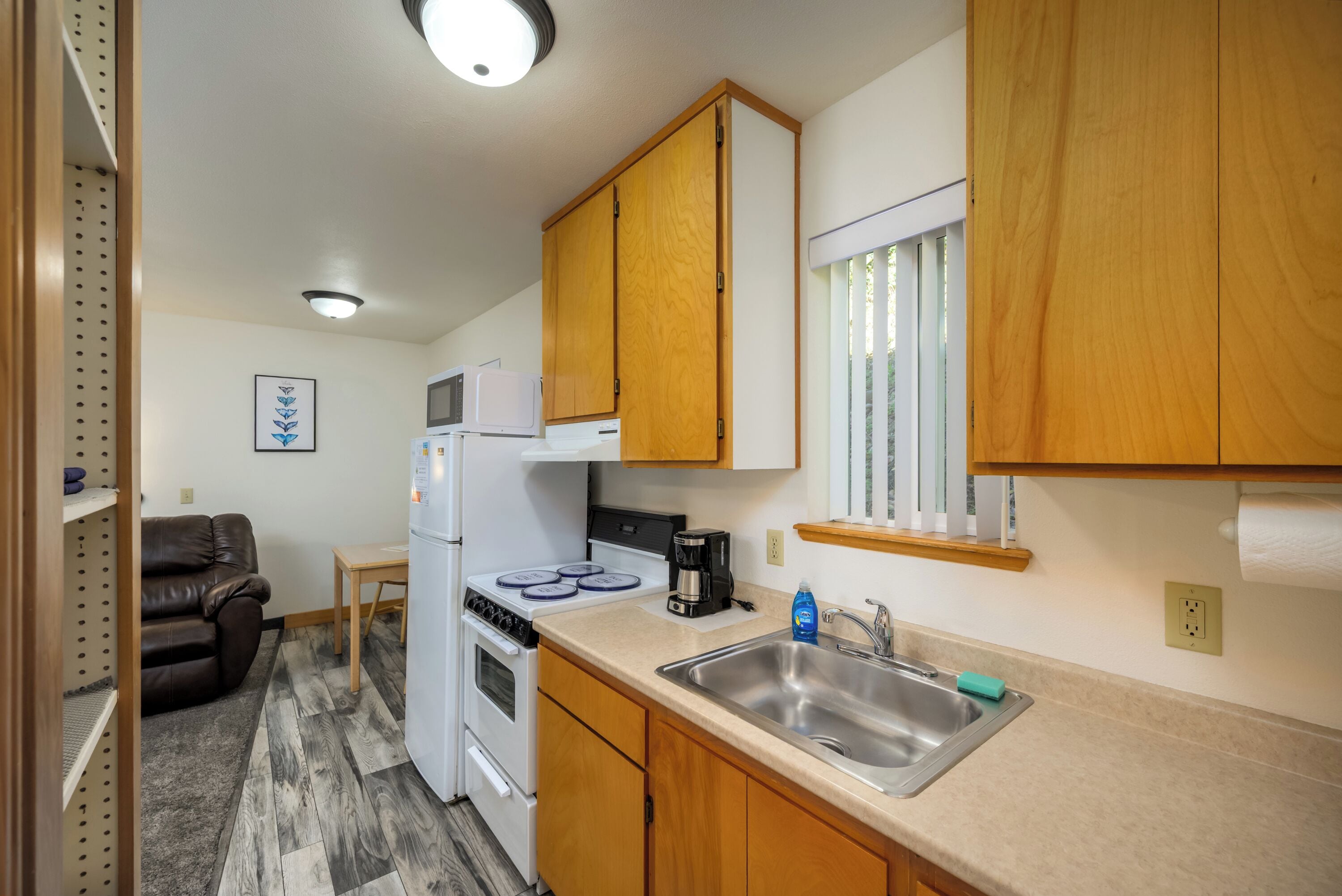 A compact kitchen with wooden cabinets, a white stove, a sink, and a window with blinds.