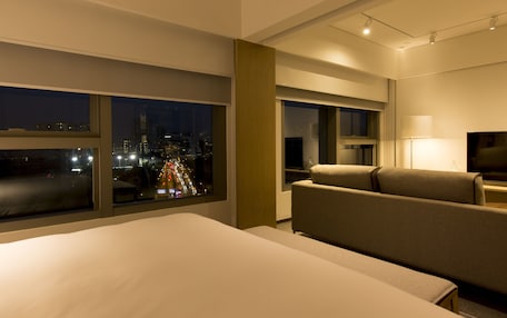 A hotel room with a large bed, a sofa, a TV, and a window with a city view at night.