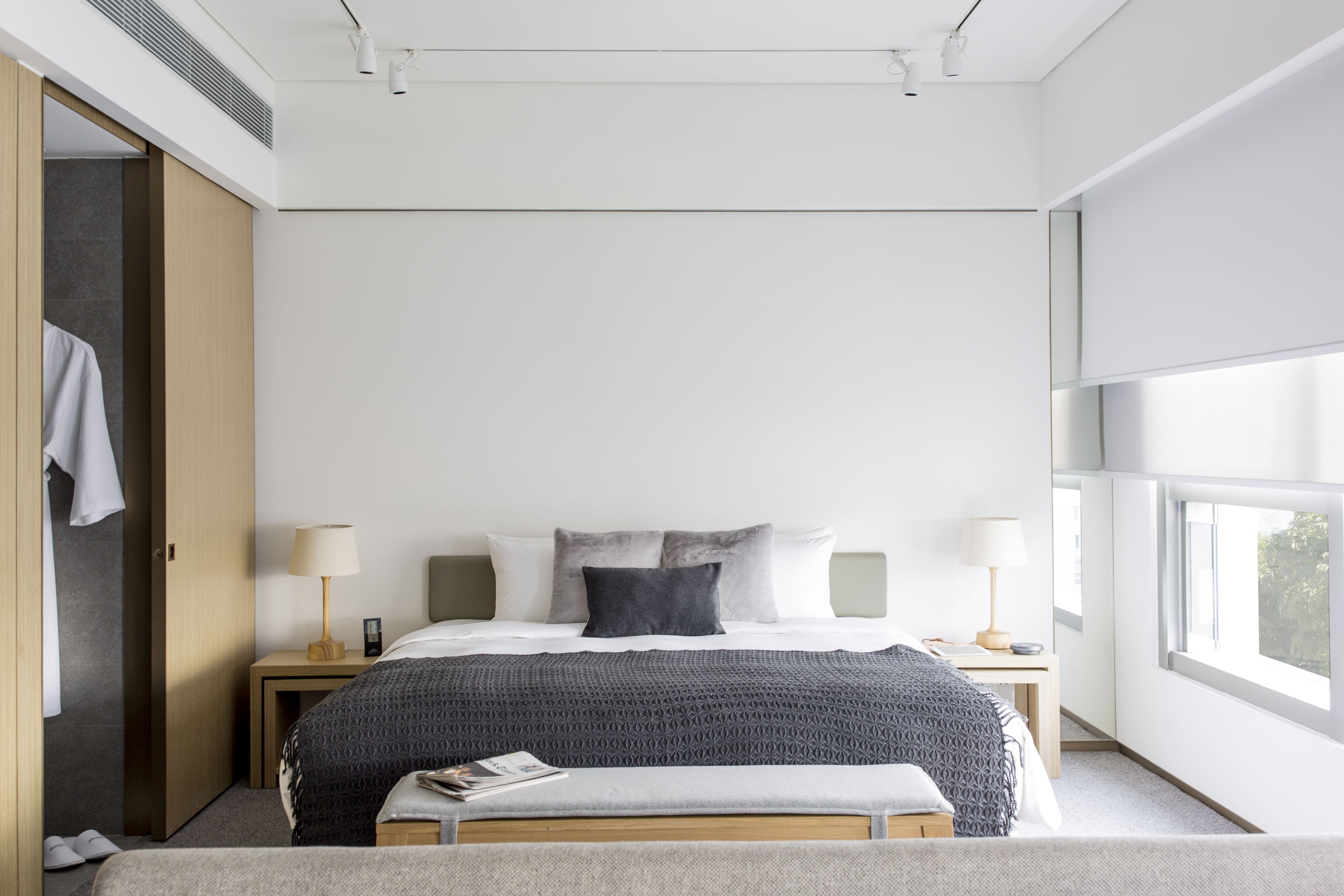 A modern hotel room with a large bed, two bedside tables, a bench, and a wardrobe.