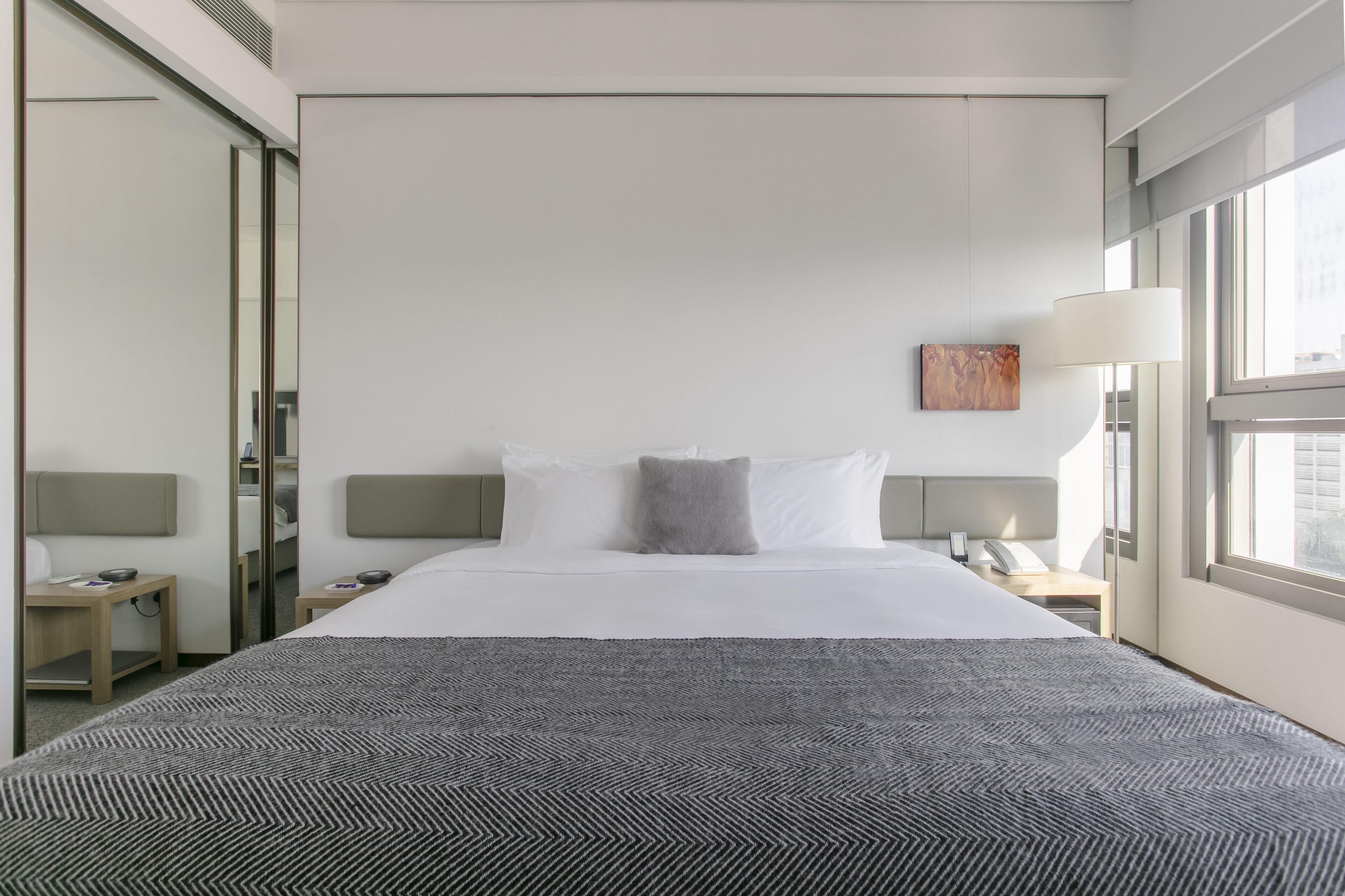 A hotel room with a large bed, a bedside table, a nightstand, a lamp, and a window.