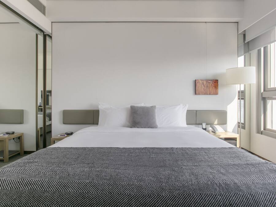 A hotel room with a large bed, a bedside table, a nightstand, a lamp, and a window.
