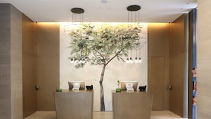 Zona de recepción con dos mostradores, cada uno con un ordenador portátil y una planta pequeña. Hay un gran árbol montado en la pared e iluminación colgante sobre los mostradores.