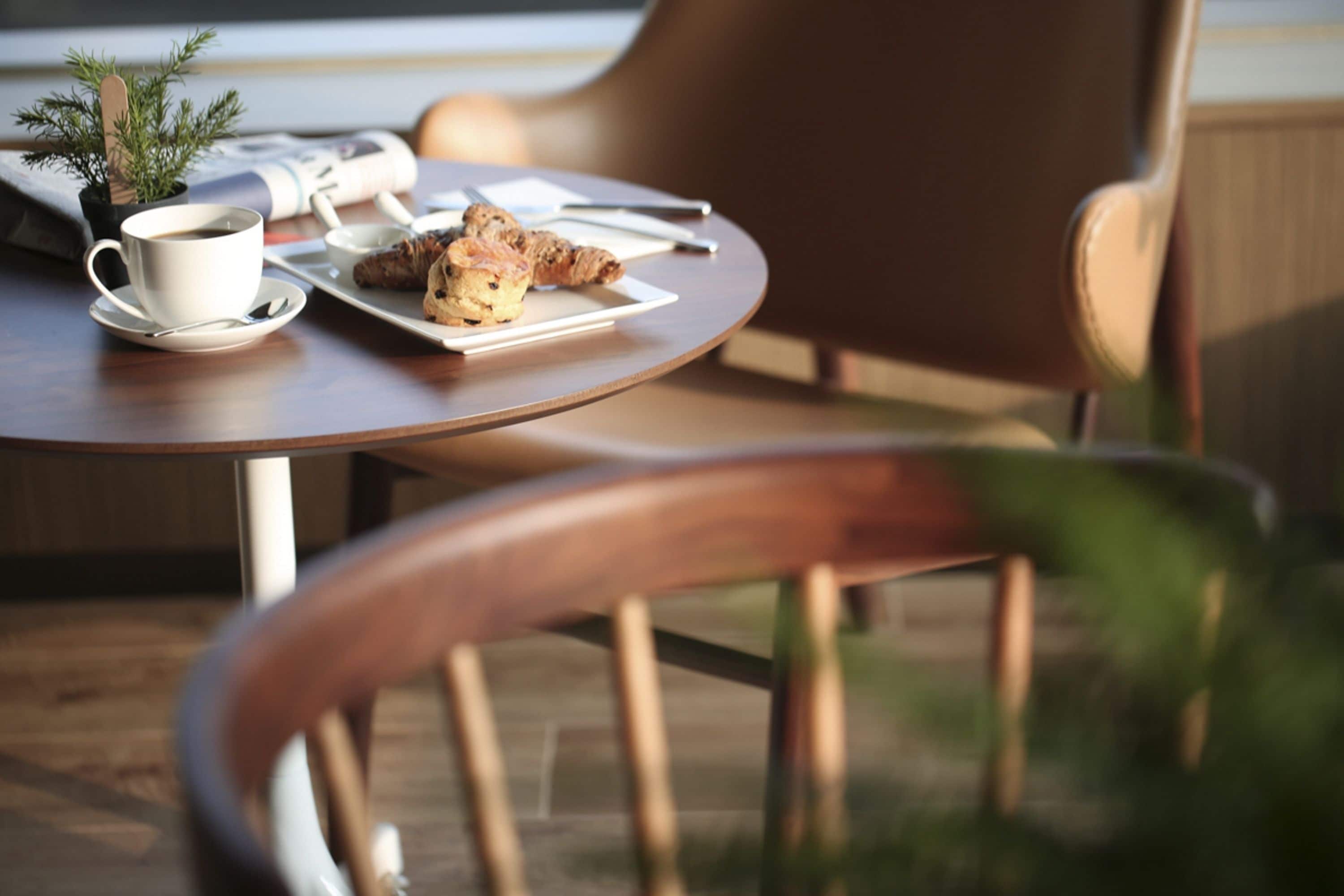 A round wooden table with a cup of coffee, a plate with pastries, and a small plant.