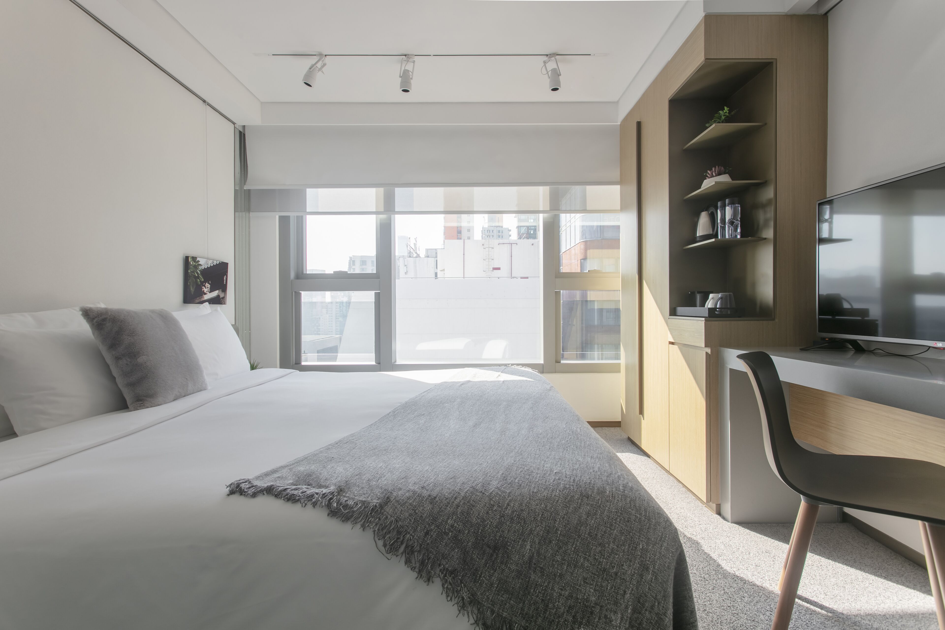 A modern bedroom with a large bed, a desk, and a TV.