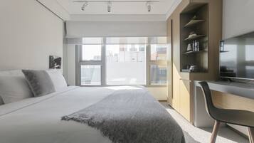 A modern bedroom with a large bed, a desk, and a TV.