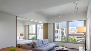 Una habitación de hotel moderna con cama, sofá, mesa de comedor y vistas de la ciudad a través de amplias ventanas.