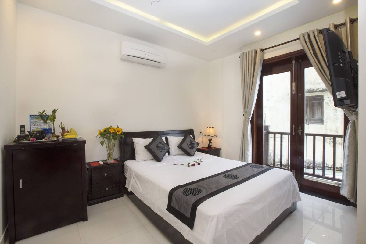 Une chambre d’hôtel avec un lit, un bureau, une télévision, une lampe et une fenêtre avec des rideaux.