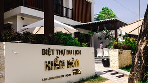 A hotel entrance with a sign in Vietnamese, a covered outdoor seating area, and a person walking in the background.