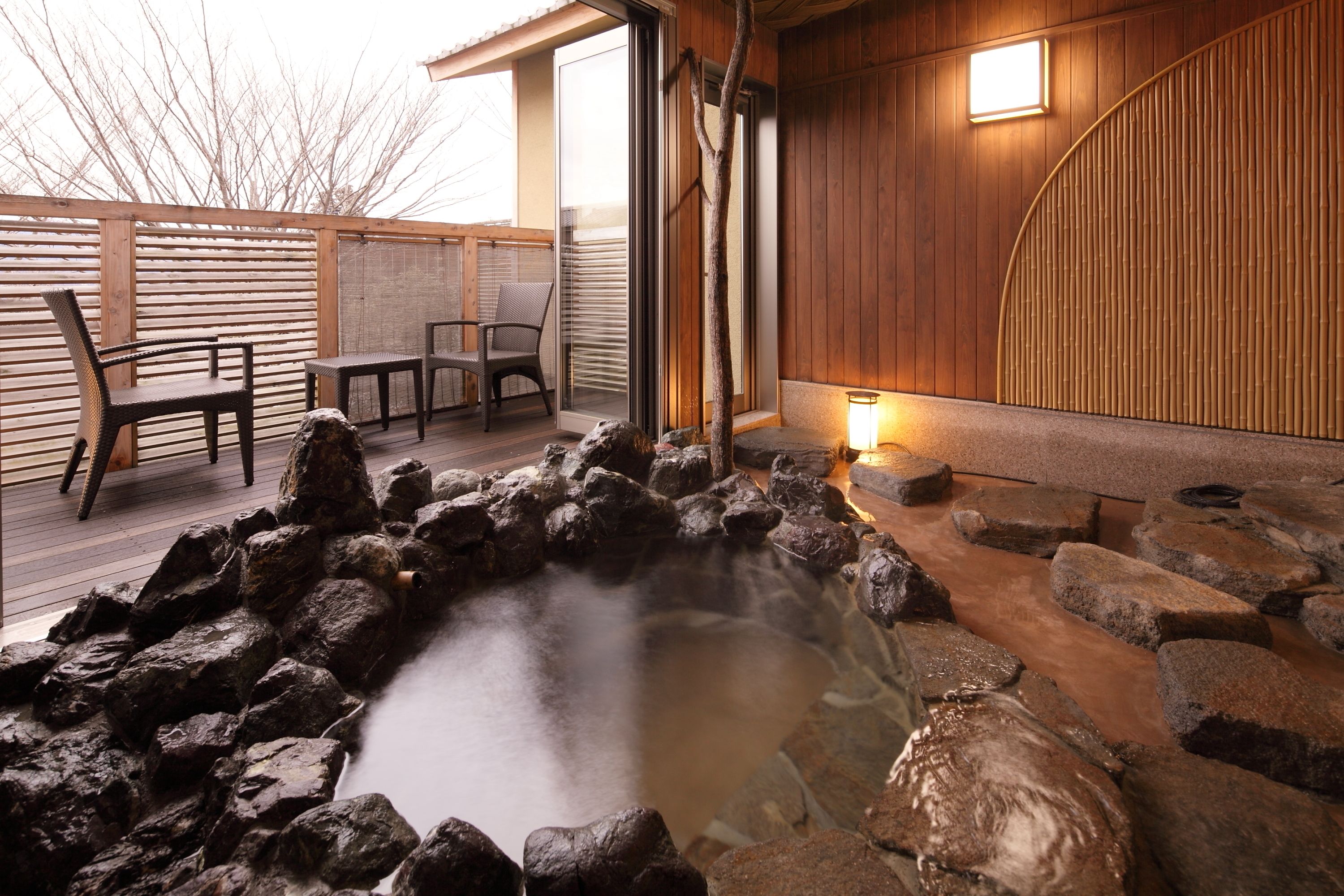 A hot spring area with a wooden deck, seating, and a stone wall.