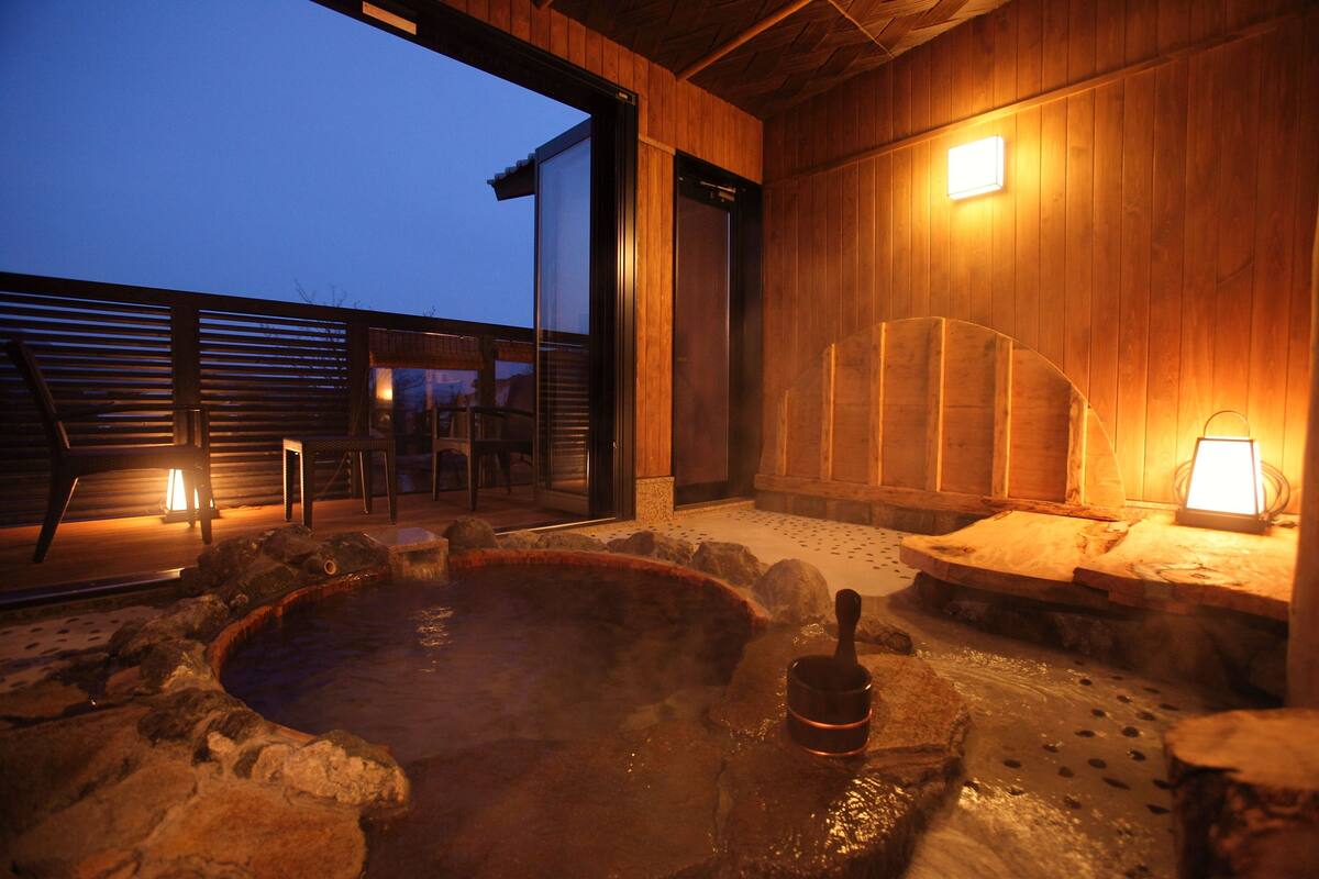Ein Thermalbadbereich mit Steinsitzen und einer Holzterrasse, beleuchtet durch Wandleuchten.