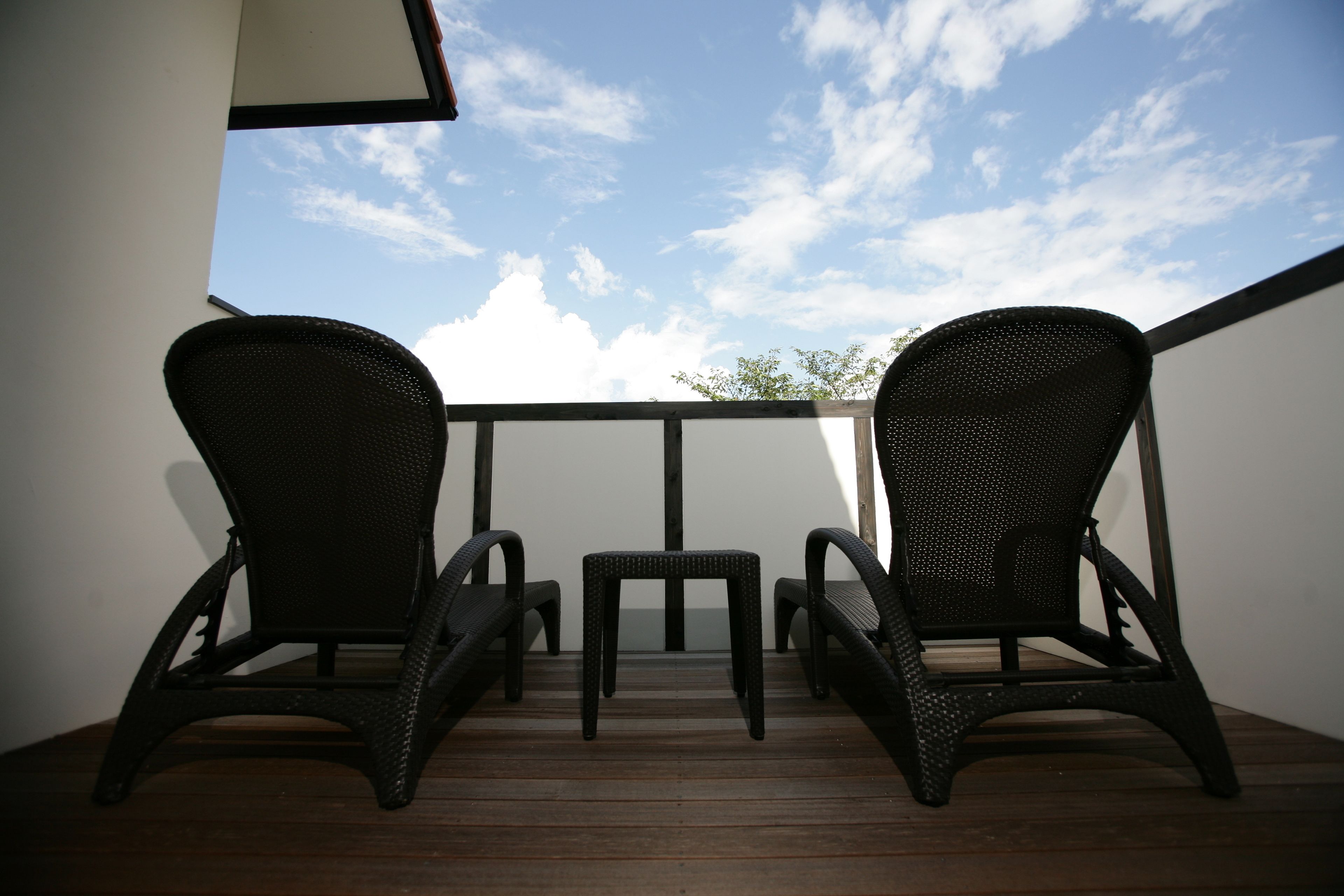Ein Balkon mit zwei Korbstühlen und einem kleinen Tisch, mit Blick auf einen wolkenlosen Himmel.