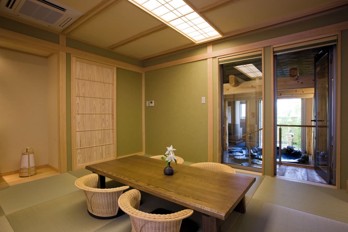 Ein traditioneller japanischer Raum mit Tatami-Boden, einem Holztisch mit Blumenvase und verschiebbaren Türen zu einem Gartenbereich.