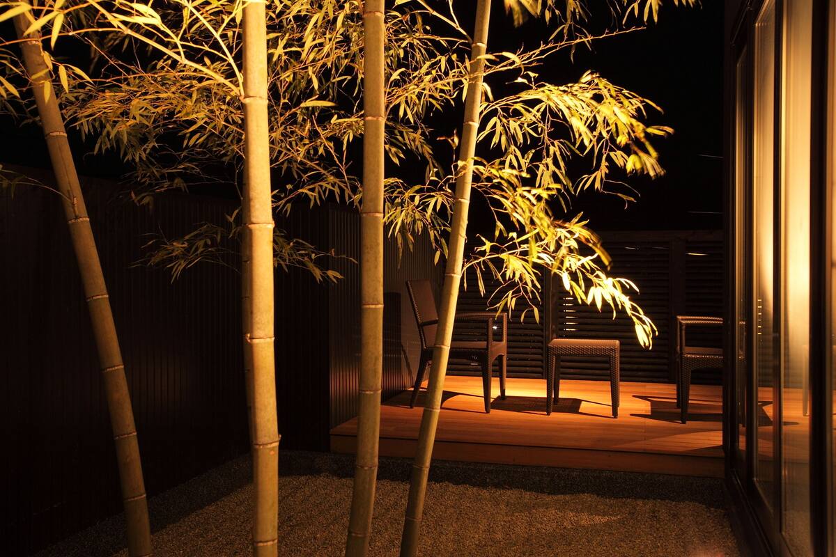 Ein Bambushain bei Nacht mit Stühlen und einem Tisch auf einer Holzterrasse.