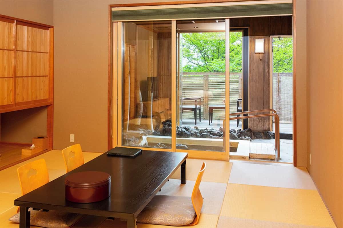 Ein traditioneller japanischer Raum mit Tatami-Böden, einer Schiebetür zu einem Außenbereich mit einer Steinsitzbank und einem Holztisch.