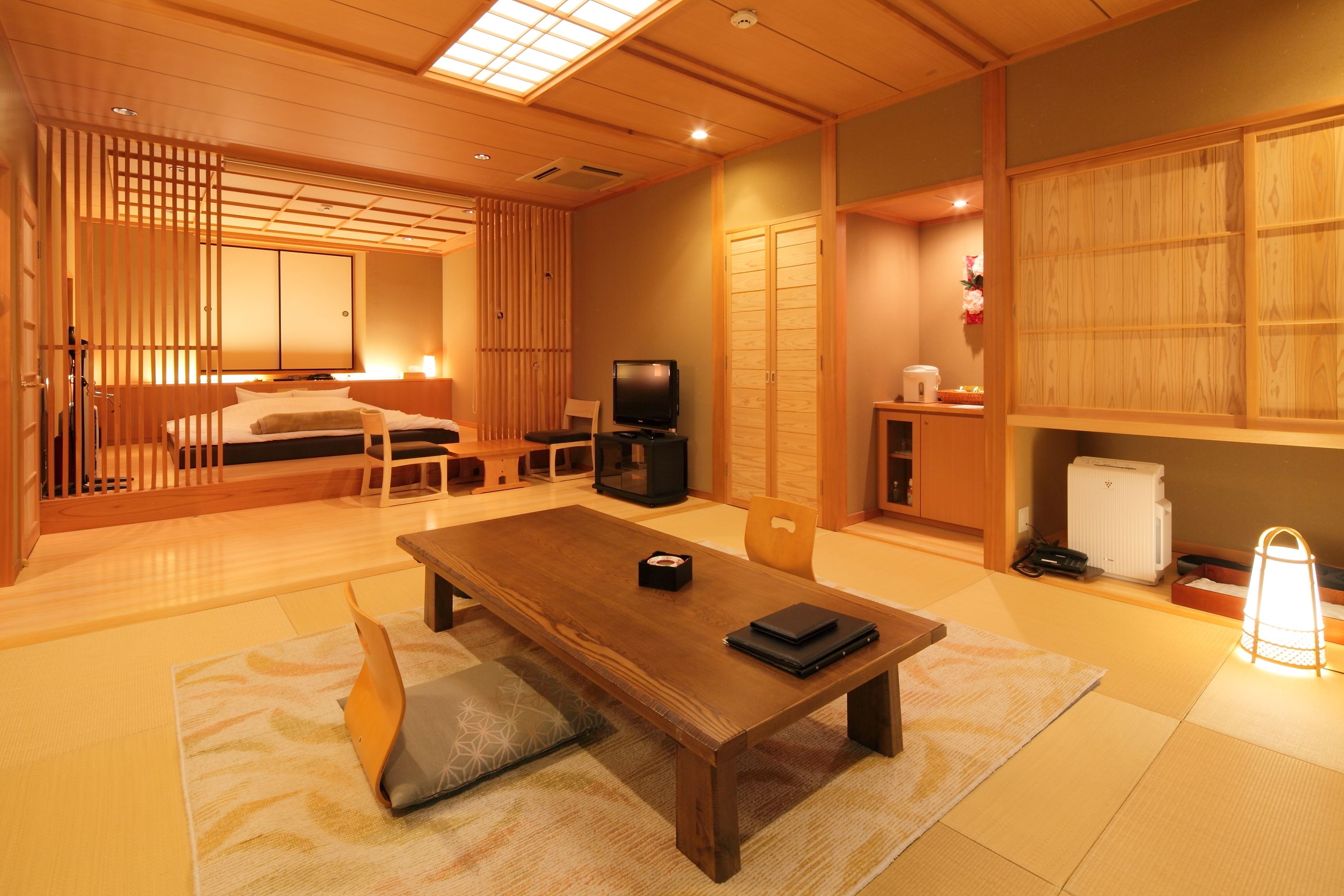 A traditional Japanese room with tatami flooring, a low wooden table, a television, and sliding doors.