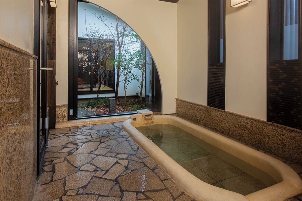 Ein Wellnessbereich mit Steinplattenboden, einer Whirlwanne und einer Glastür zum Garten.