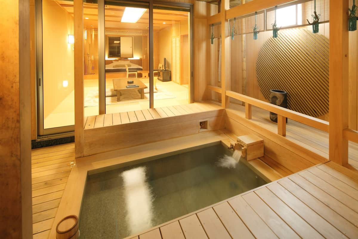 Ein traditionelles japanisches Onsen mit einer Holzdachterrasse, einem Thermalbad und einem Raum mit Tatami-Matten.