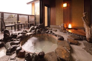 A hot spring area with a stone pool surrounded by rocks, wooden deck, and a seating area with chairs and a table. - Bettei Soan (Minamiaso)