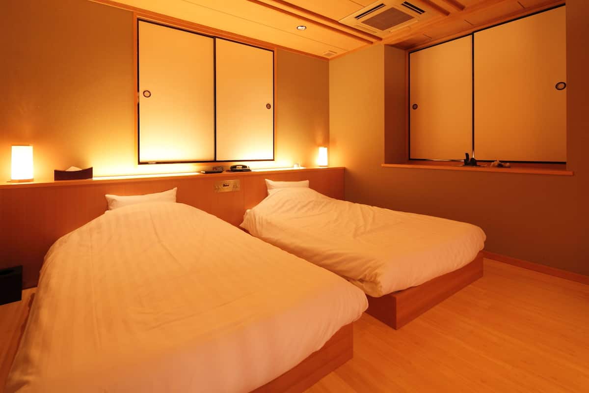 Ein Hotelzimmer mit zwei Einzelbetten, Holz-Kopfteilen und einer großen Schiebetür.
