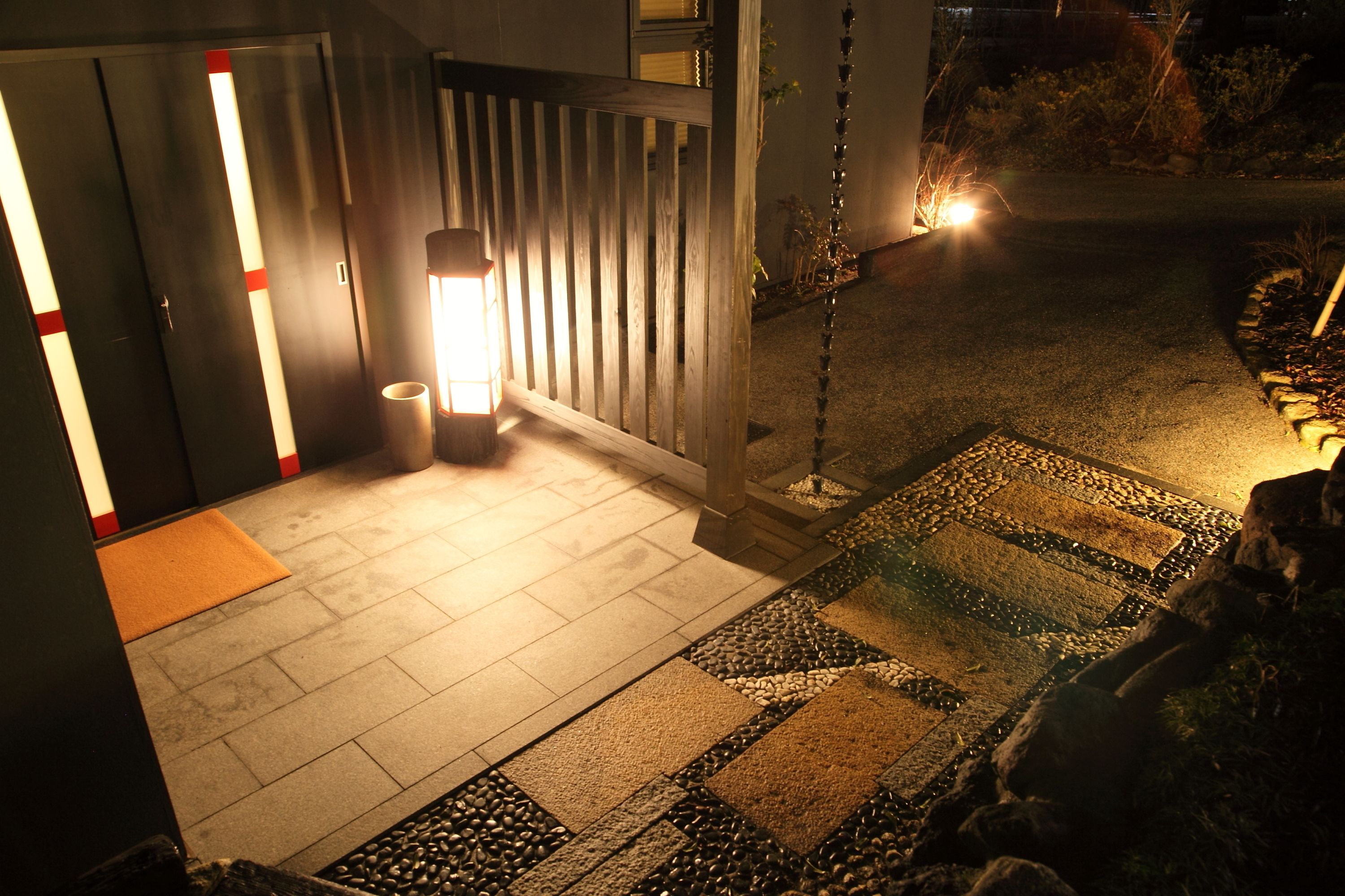 A well-lit entrance with a wooden gate, a stone pathway, and a small garden area.