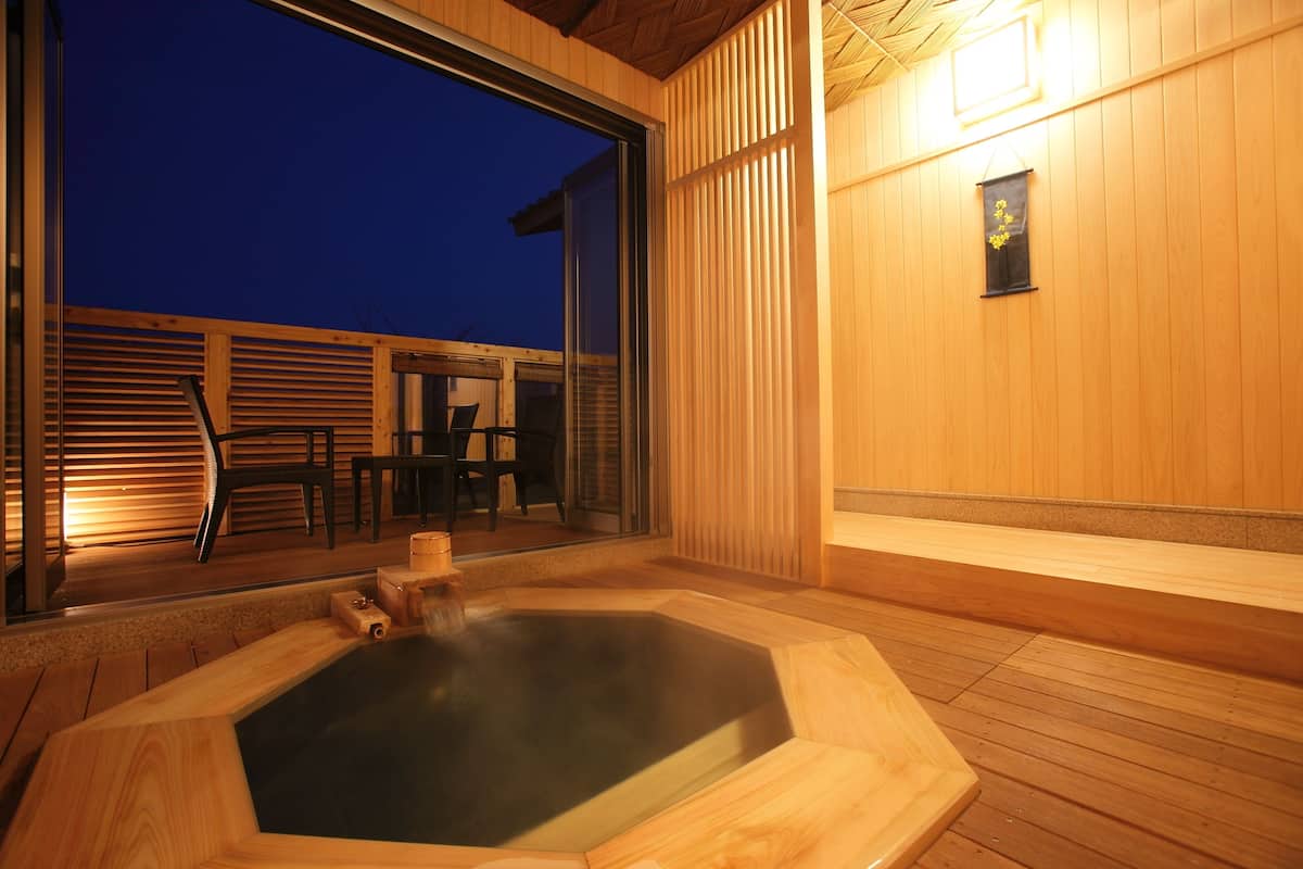 Eine Holzterrasse mit Whirlpool, Holzwänden und einer Sitzgruppe mit Stühlen und Tischen.