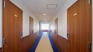 A long hallway with wooden doors on both sides, a blue carpet, and a ceiling light. - HOTEL LiVEMAX BUDGET Kawasaki Daishi (Kawasaki)