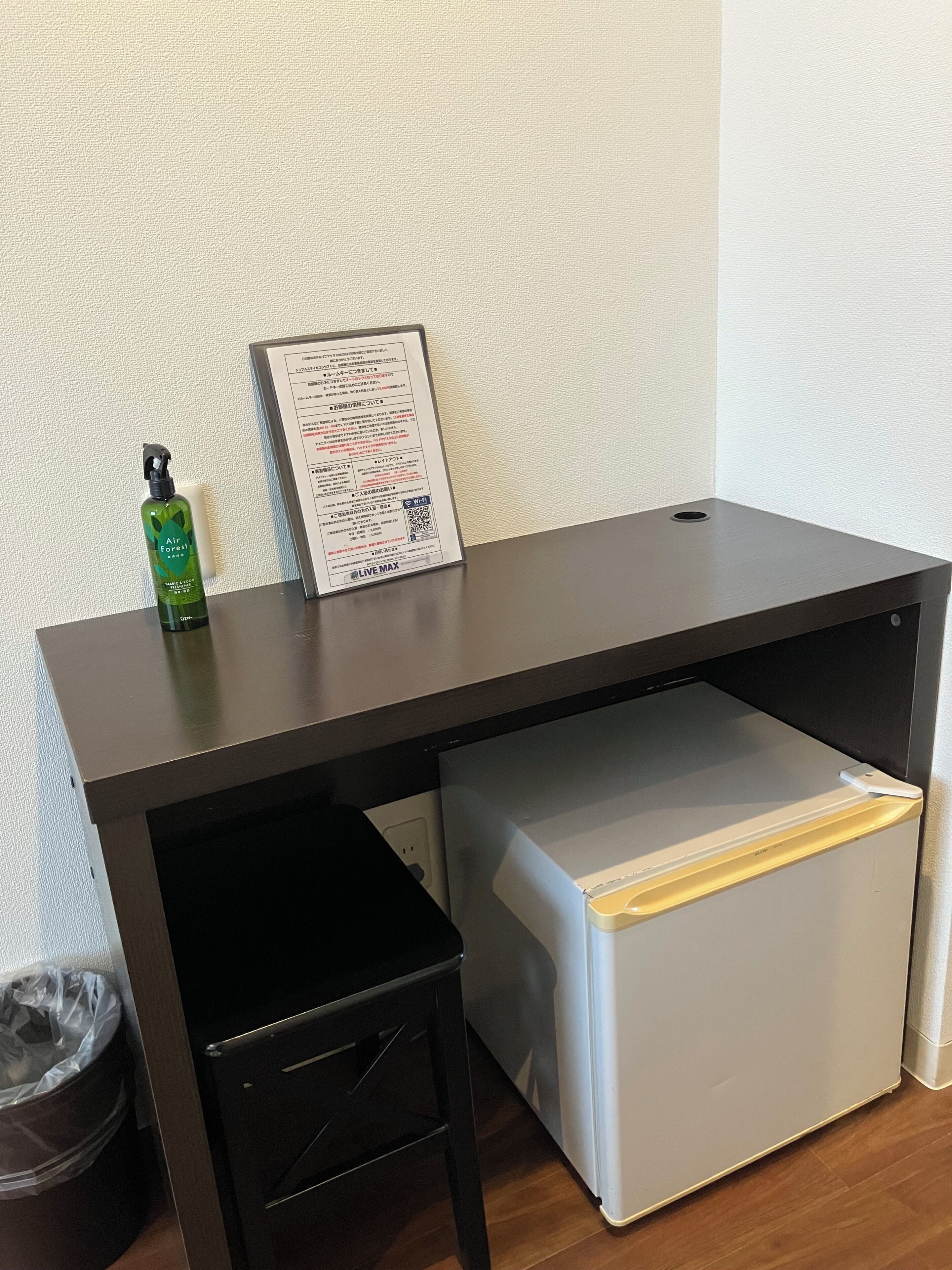 Un bureau avec un bloc-tiroirs, une poubelle et un document encadré accroché au mur.