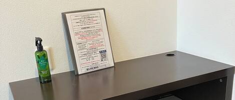 Un escritorio con una cajonera, un cubo de basura y un documento enmarcado en la pared.
