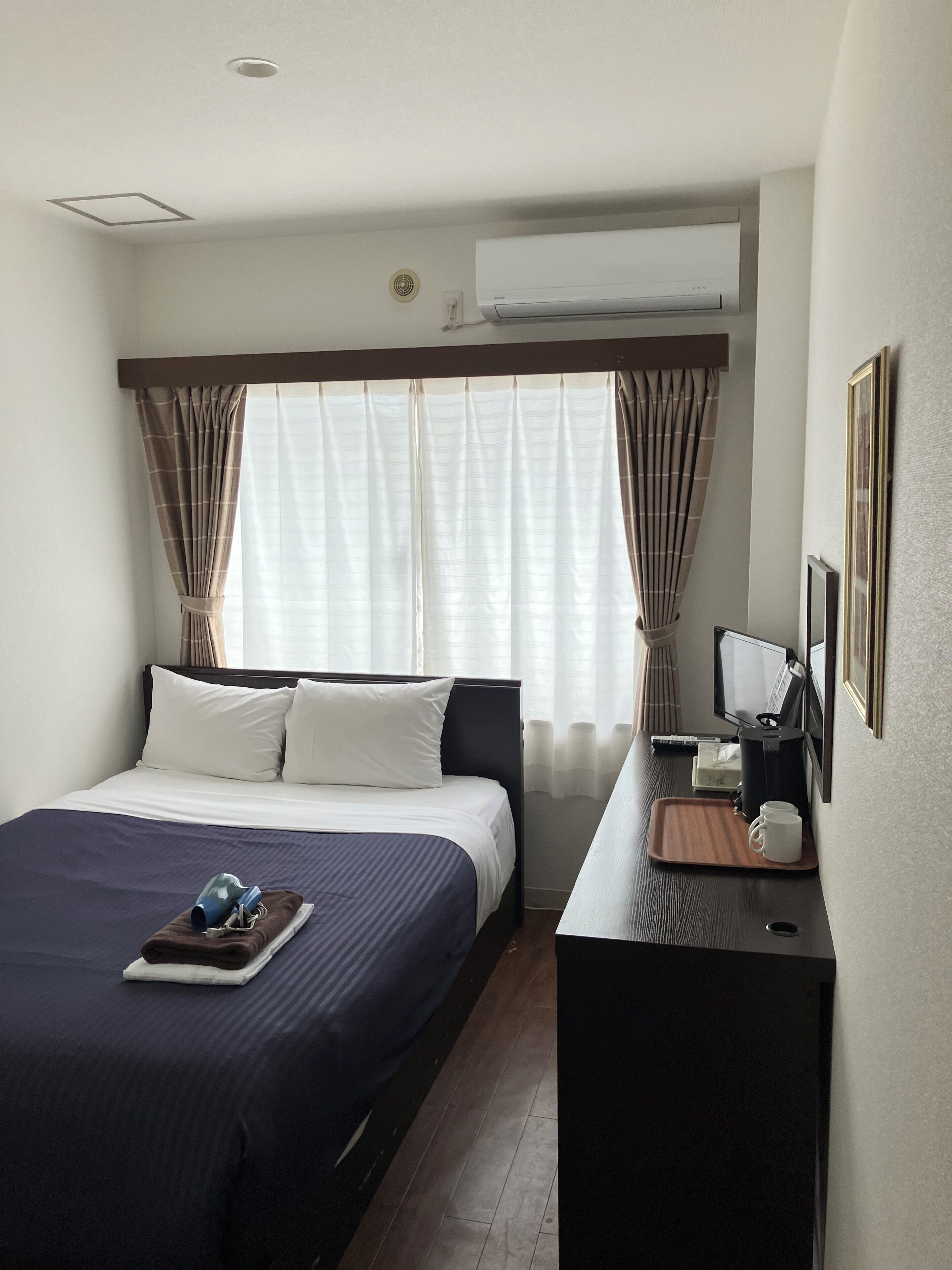 A hotel room with a bed, bedside table, and a desk with a chair.