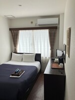 A hotel room with a bed, bedside table, and a desk with a chair.