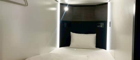 A modern hotel room with a neatly made bed, a hanging light fixture, and a visible control panel on the wall.