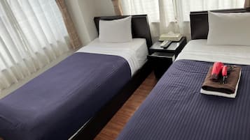 Une chambre d’hôtel avec deux lits, une table de chevet avec un téléphone et une télécommande, et une fenêtre avec des rideaux légers.