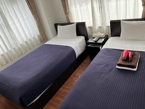 A hotel room with two beds, a nightstand with a phone and remote, and a window with sheer curtains. - HOTEL LiVEMAX BUDGET Kawasaki Daishi (Kawasaki)