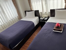 Habitación de hotel con dos camas, una mesita de noche con teléfono y control remoto, y ventana con cortinas translúcidas.