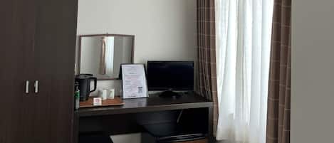 Habitación de hotel compacta con escritorio, una silla, un bote de basura pequeño, televisor y equipo de aire acondicionado.