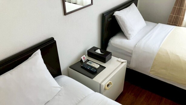 Two single beds with white linens, a bedside table with a tissue box, a remote control, and a wall-mounted mirror. - HOTEL LiVEMAX BUDGET Kawasaki Daishi (Kawasaki)