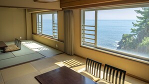 A room with tatami mats, a low table, and chairs, with large windows offering a view of the sea and a tree. - Hotel New Akao (Atami)
