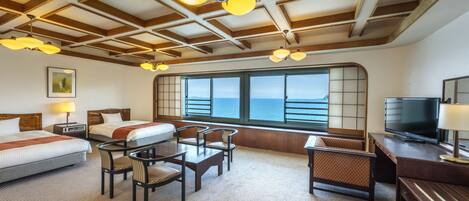 Habitación de hotel con dos camas, televisión, escritorio y un ventanal con vista al mar.