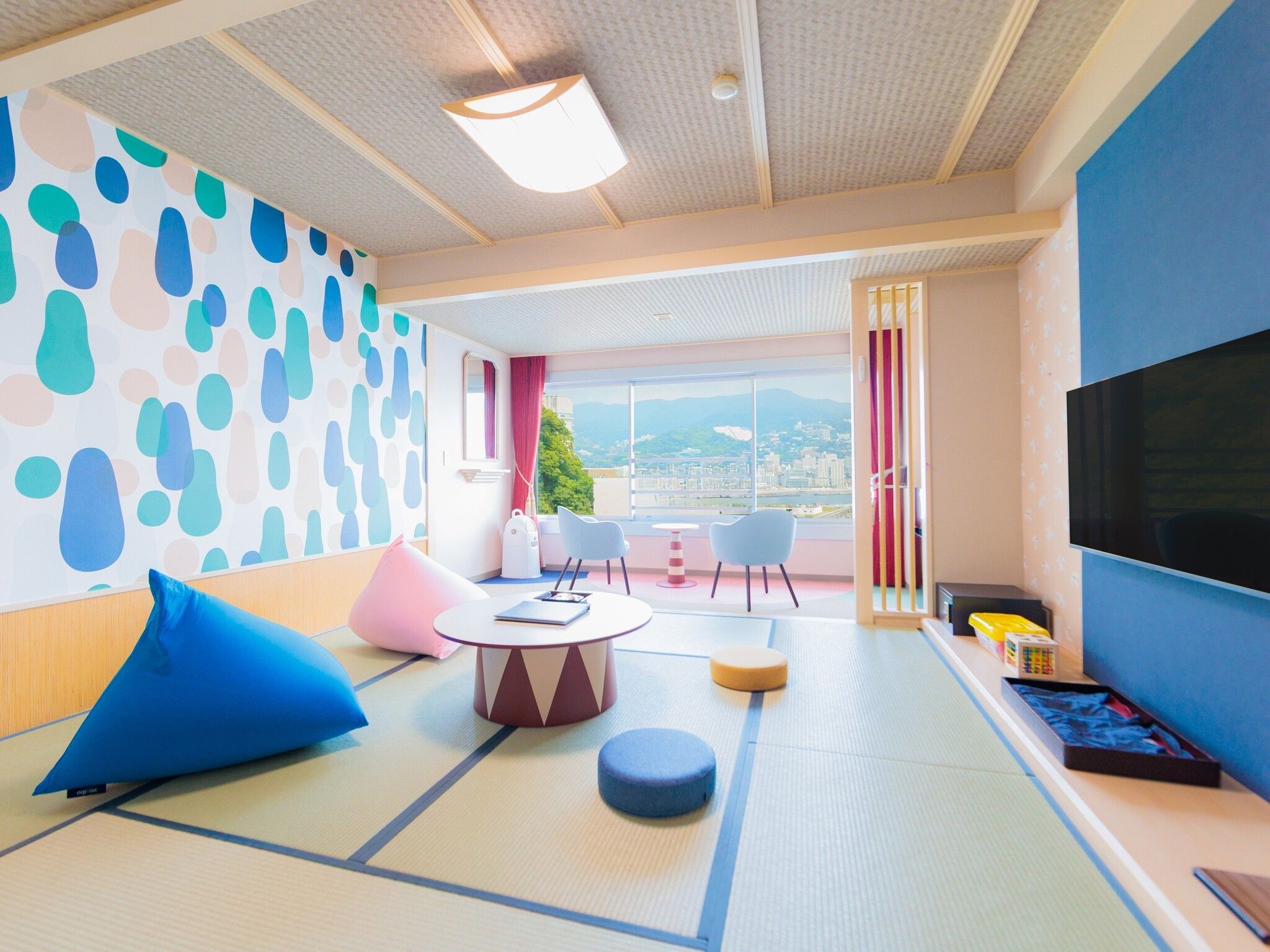 Quarto de hotel moderno com piso de tatame, uma televisão grande e varanda com vista para a cidade.