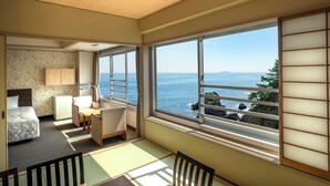 A room with a bed, a desk, a chair, and a view of the sea through large windows. - Hotel New Akao (Atami)