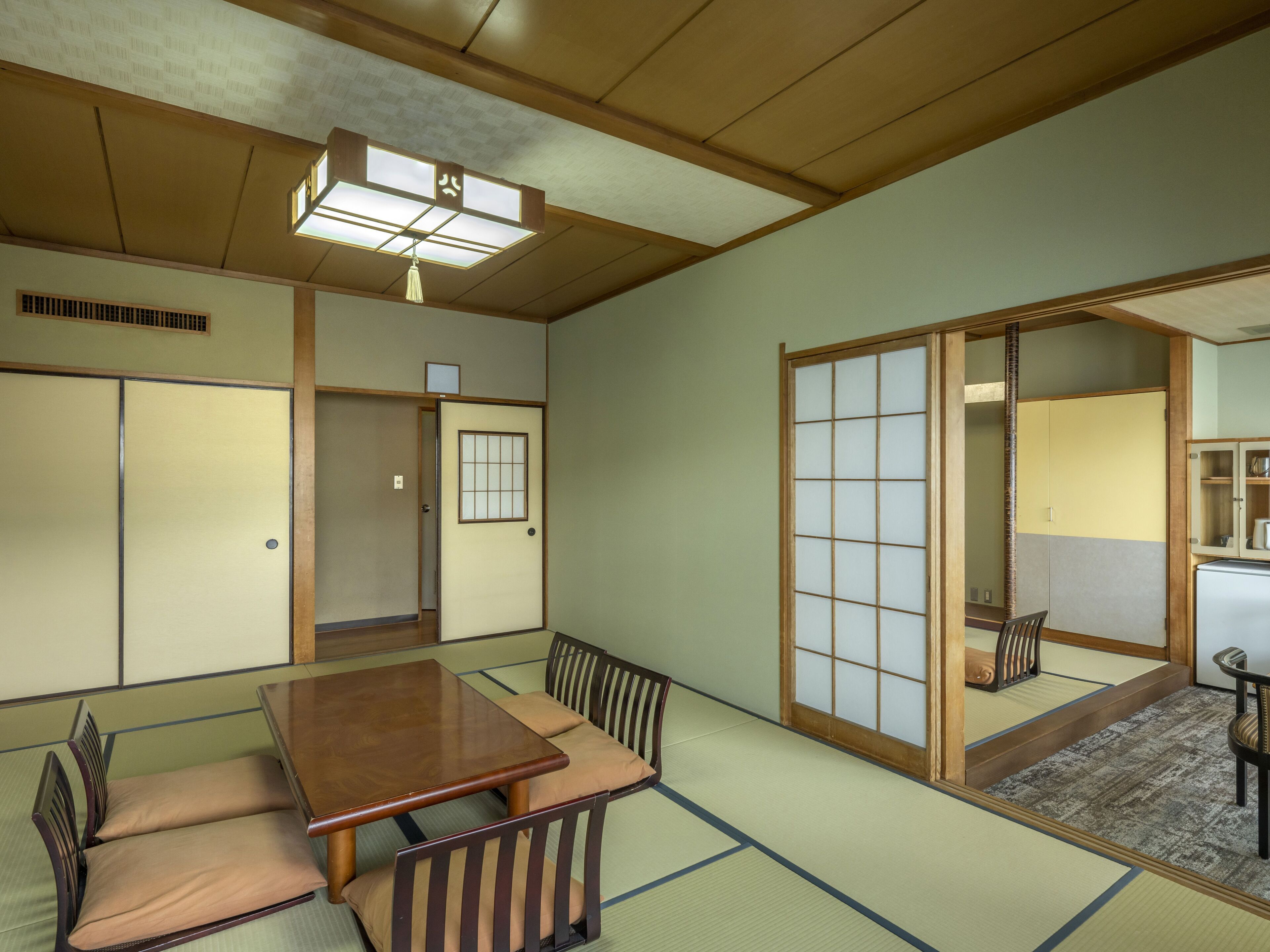 A traditional Japanese room with tatami flooring, a wooden table with cushions, sliding doors, and a ceiling light fixture.